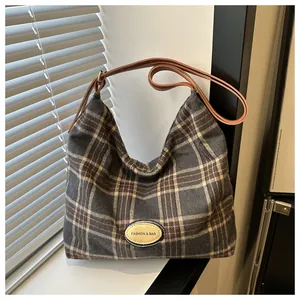 Détail du sac hobo à carreaux gris-brun avec bandoulière cuir et écusson mode