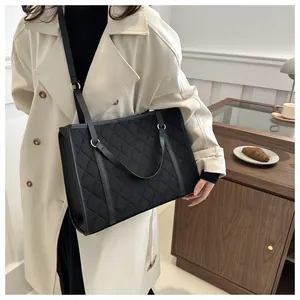 Detail of a large black quilted tote bag styled with a beige trench coat for a modern look