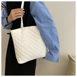 Detail of white quilted tote bag with diamond stitching texture and slender shoulder straps