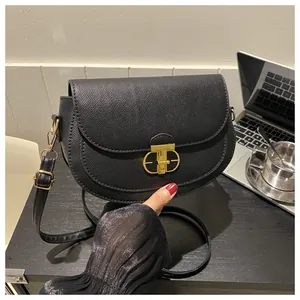 Detail of minimalist black saddle bag with textured leather and gold metal lock buckle