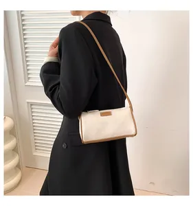Sac cylindre en toile beige chic avec bordure en cuir marron porté à l'épaule