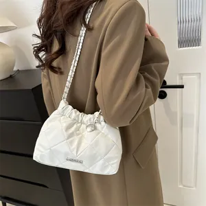 Sac seau matelassé blanc moderne avec chaîne argentée porté par une femme en blazer