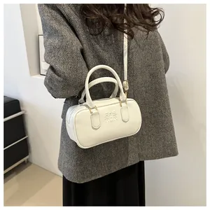Detail of white cylinder bag featuring FASHION embossing and gold-tone hardware on model
