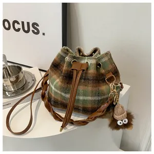 Detail of vintage plaid bucket bag with plush monster charm and leather drawstring