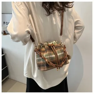 Detail of checkered drawstring bucket bag with leather strap and plush pompom accessory