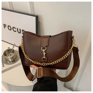 Détail du sac en cuir marron foncé avec chaîne dorée et large bandoulière en tissu