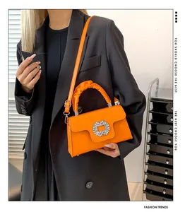 Close-up of bright orange crossbody bag featuring a sparkling crystal buckle and ruched handle