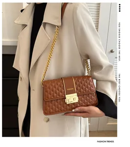 Detail of a brown quilted crossbody bag with a gold chain strap and metal clasp