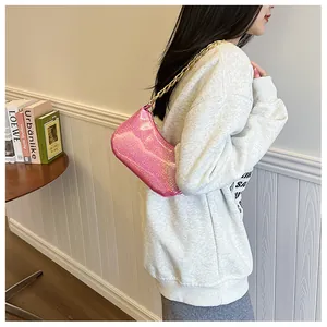 Detail of pink sequin crescent bag with gold chain strap worn by a model in a stylish room