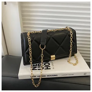 Detail of black quilted crossbody bag with golden chain and metallic buckle on white books