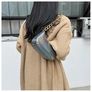 Close-up of holographic underarm bag with thick gold chain strap on knit cardigan