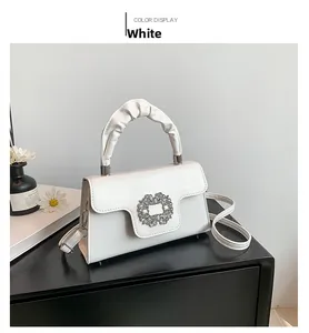 Detailed view of white crossbody bag with sparkling rhinestone buckle and ruched handle