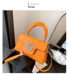 Detail view of orange handbag with rhinestone buckle and stylish ruched handle