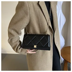 Detailed close-up of black quilted shoulder bag with gold chain strap on model