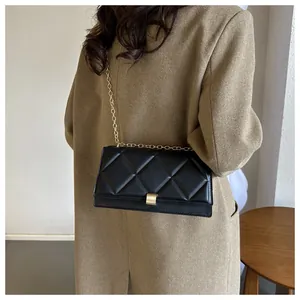 Detail of a black quilted shoulder bag with gold chain and metal lock on a khaki coat
