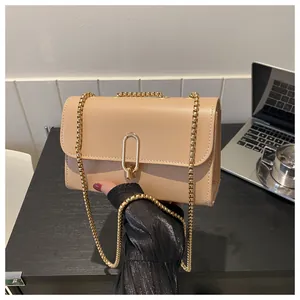 Detail of minimalist beige crossbody bag with gold chain strap on an office desk