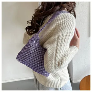 Nahaufnahme einer lila Strass-Umhängetasche mit Netzmuster und beige Strickpullover-Detail