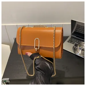 Detail of a brown leather crossbody bag with white stitching and a gold metal clasp