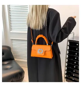 Detail of orange matte leather handbag with rhinestone buckle on a black blazer