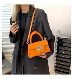 Close-up of bright orange crossbody bag with crystal buckle and ruched handle detail