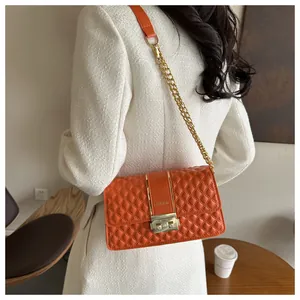 Detail of orange quilted crossbody bag with gold chain strap and fashion clasp hardware