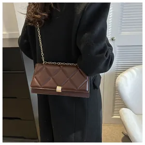 Detail of a dark brown quilted shoulder bag with gold chain strap on a black coat