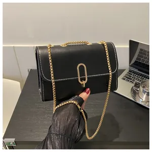 Detail of black leather crossbody bag with gold chain strap and decorative white stitching