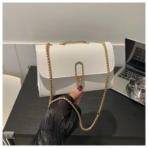 Detail of white faux leather crossbody bag with gold oval clasp and fine metal chain