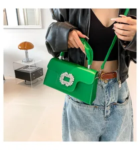 Close-up of a green handbag with a sparkling rhinestone buckle on a black jacket model
