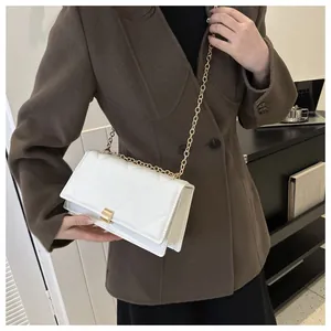 Close-up of white quilted crossbody bag with gold chain strap on dark brown blazer