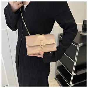 Detail of a beige leather crossbody bag with a golden oval metal clasp and chain strap