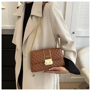 Detail of a brown quilted crossbody bag with gold chain and metal buckle on beige coat