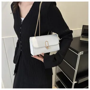 Close-up of white crossbody bag with gold U-shaped lock on a chic black dress