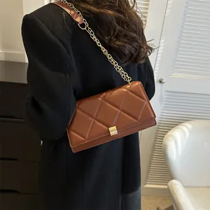 Brown quilted crossbody bag with gold chain strap shown on a model in a black coat