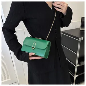 Detail of green leather shoulder bag with gold U-shaped buckle and metal chain strap