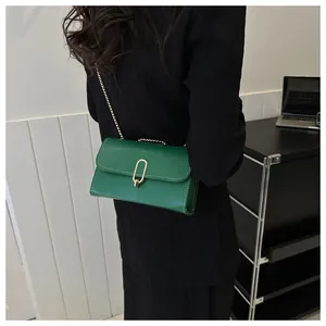 Detailed view of emerald green leather crossbody bag with golden metal chain and oval clasp