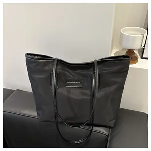 Detail view of black oxford fabric tote with leather brand tag and thin shoulder strap