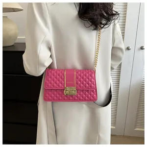 Close-up of fuchsia quilted crossbody bag with gold chain strap on a white coat