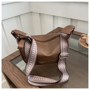 Dettaglio borsa a mezzaluna marrone con ampia tracolla geometrica in stile bohémien