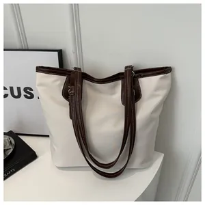 Detail of high-capacity canvas tote bag showing contrast stitching and brown leather strap
