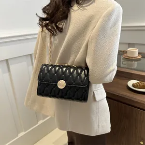 Elegante schwarze Stepptasche mit goldener Kette getragen zum schicken Tweed-Blazer