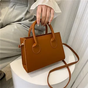 Brown rectangular crossbody bag with dual top handles and gold hardware on white display