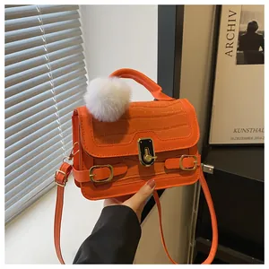 Detail der orangefarbenen Tasche mit Krokoprägung, Goldverschluss und Plüschanhänger