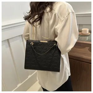 Detail of a black geometric embossed handbag with gold chain strap on a female model