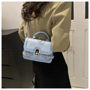 Detail der hellblauen Kroko-Handtasche am Model mit goldenen Beschlägen und Gurt