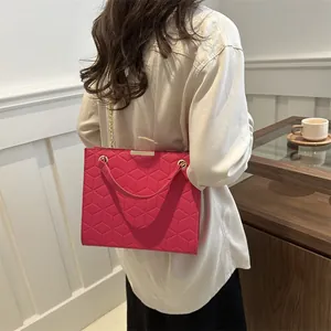 Pink crossbody bag with geometric quilting and gold chain strap worn by a model