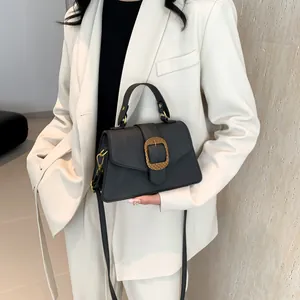 Minimalist black matte leather crossbody bag with an oval gold buckle on a beige suit