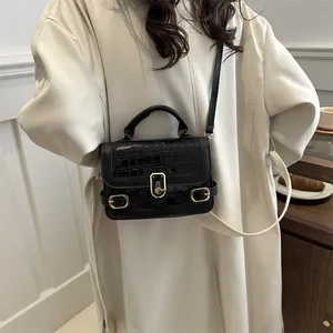 Elegante schwarze Handtasche mit Steinstruktur und Goldschnalle auf beigem Trenchcoat