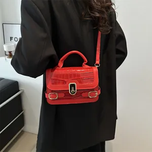 Rote Umhängetasche mit Kroko-Prägung und Goldschnalle an Model mit schwarzem Mantel