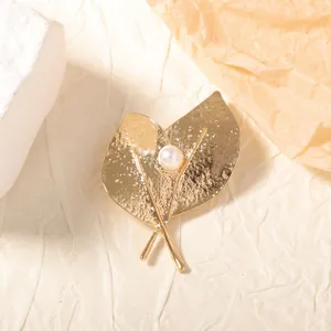 Gros plan détaillé d'une broche feuille dorée avec texture martelée et perle blanche